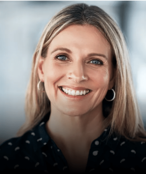 Professional headshot of smiling woman with long blonde hair in dental office setting.