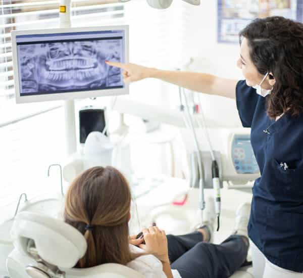 Dentist pointing at digital scan on monitor while patient sits in dental chair.