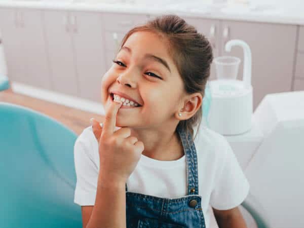 Young girl smiling in bathroom, brushing teeth at sink with toothbrush.