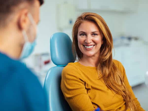 Woman in yellow shirt smiling at dentist in blue scrubs during dental office consultation.