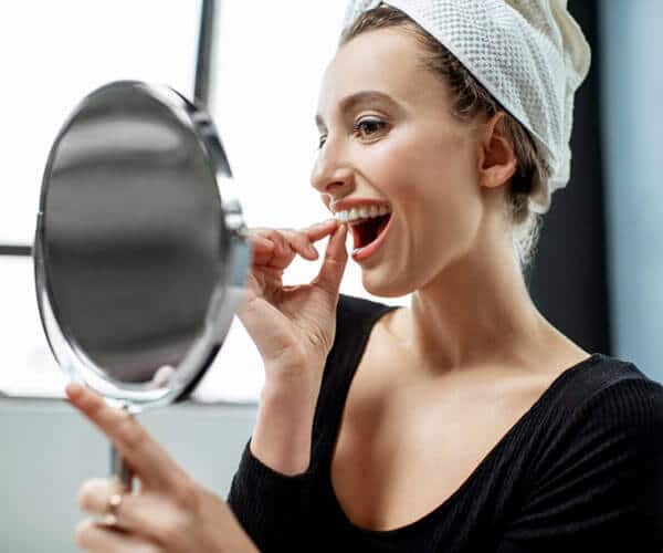 Woman with headband applying red lipstick while looking in handheld mirror indoors.