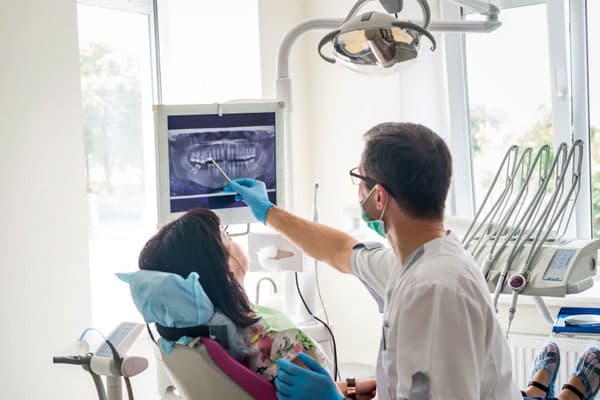 Dentist examining patient's teeth in modern dental office with overhead light and equipment visible.