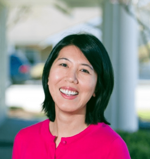 Woman in pink shirt smiling at camera, dental office setting with blurred background.