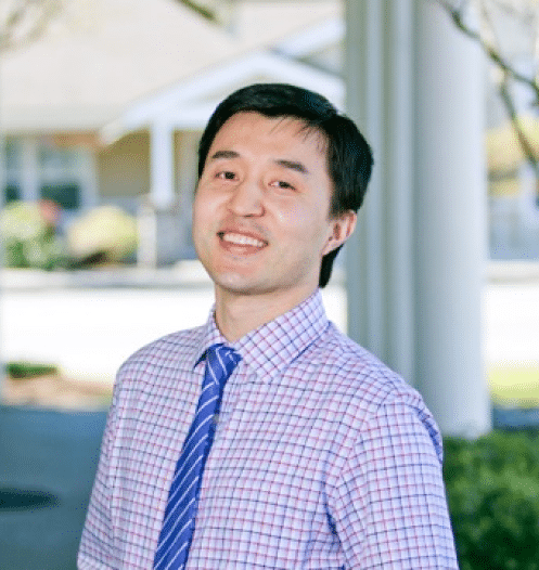 Professional smiling in blue checkered shirt and tie at dental office.