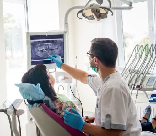 Dentist examining patient's teeth in modern dental office with overhead light and equipment.