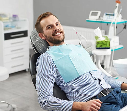 Man reclined in dental chair at Shelton Dental Excellence office with bib, smiling at camera.