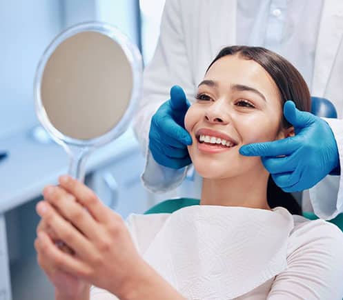 Patient admiring smile in dental mirror after treatment at Shelton Dental Excellence office