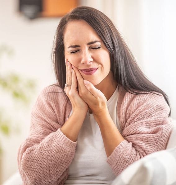 Woman experiencing tooth pain, holding her cheek, in a bright home setting.