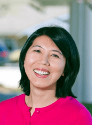 Woman in pink top smiling at camera in bright dental office setting.