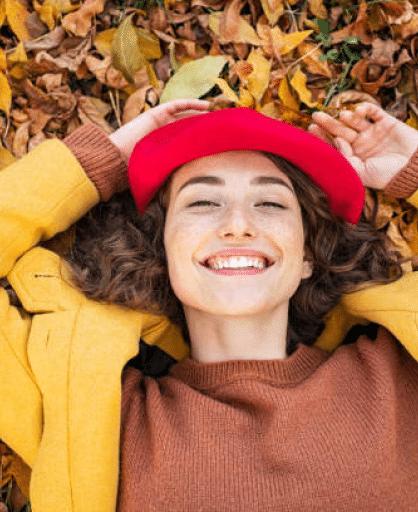 Smiling woman lying in fall leaves wearing red hat and yellow jacket