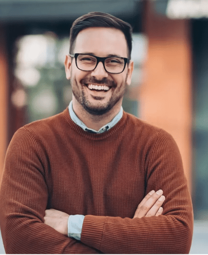 Smiling male dental professional wearing glasses and rust-colored sweater in modern office setting.